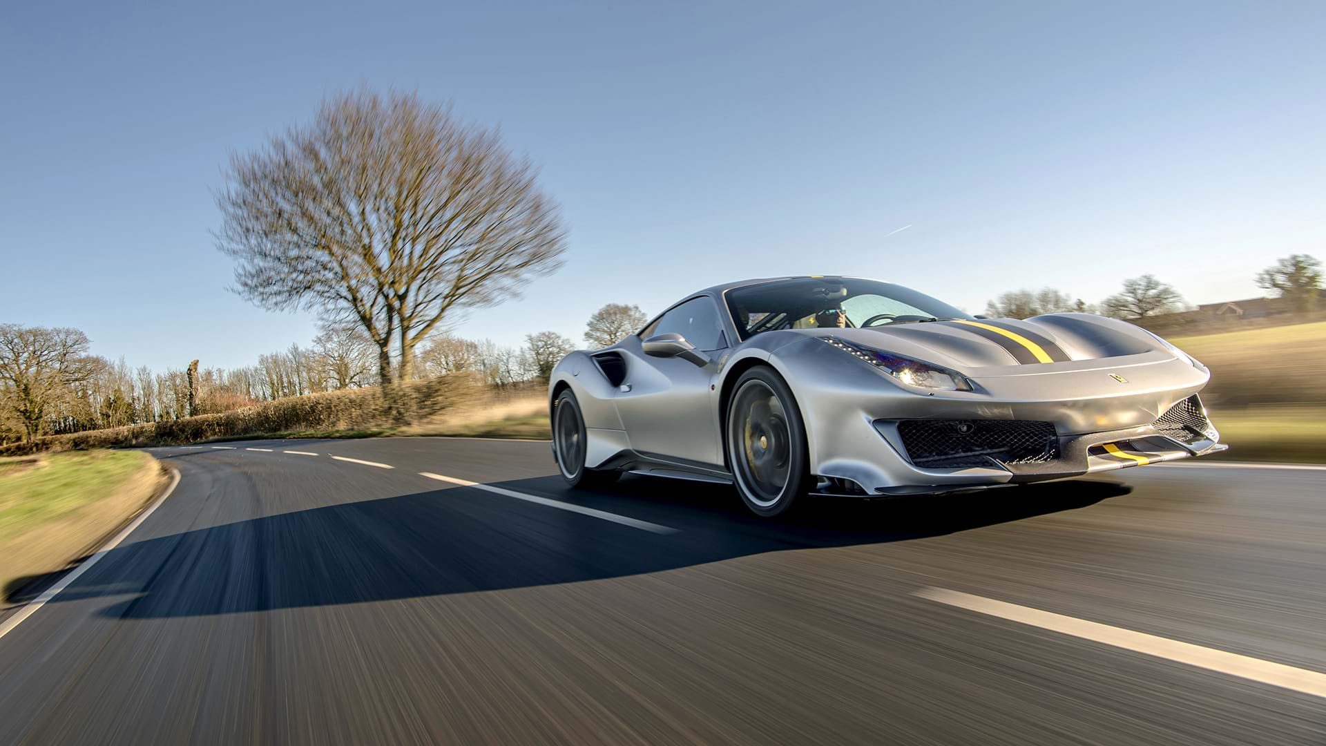 Elegante pista grigia Ferrari 488 con un'audace striscia da corsa che sfreccia attraverso uno scenografico paesaggio di campagna. 