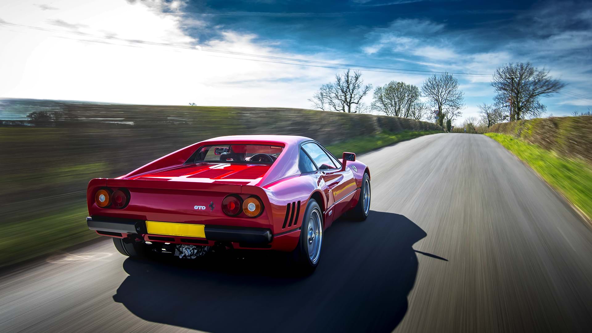 Classica Ferrari 288 GTO rossa che sfreccia lungo una strada di campagna panoramica. 