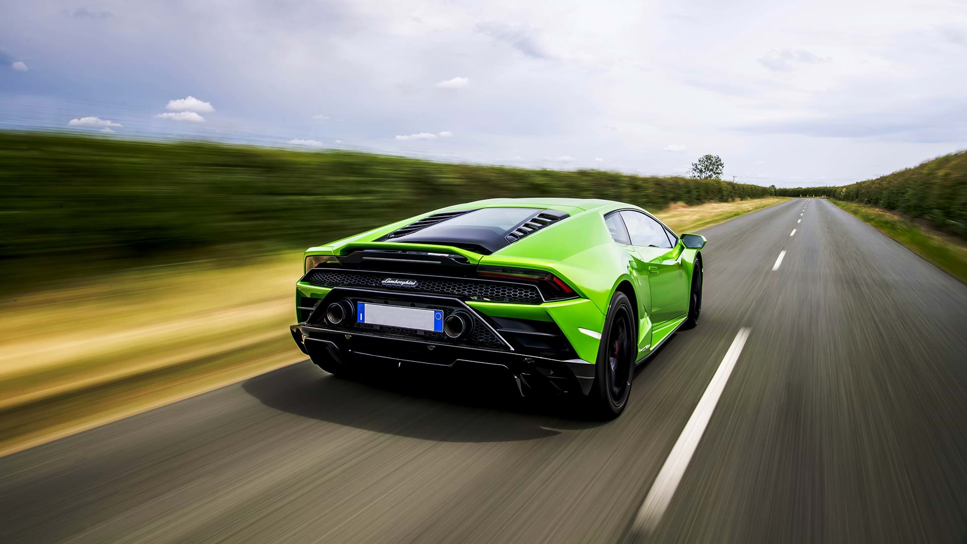 Huracán Evo Lamborghini verde brillante che sfreccia lungo una strada di campagna in una giornata di sole.
