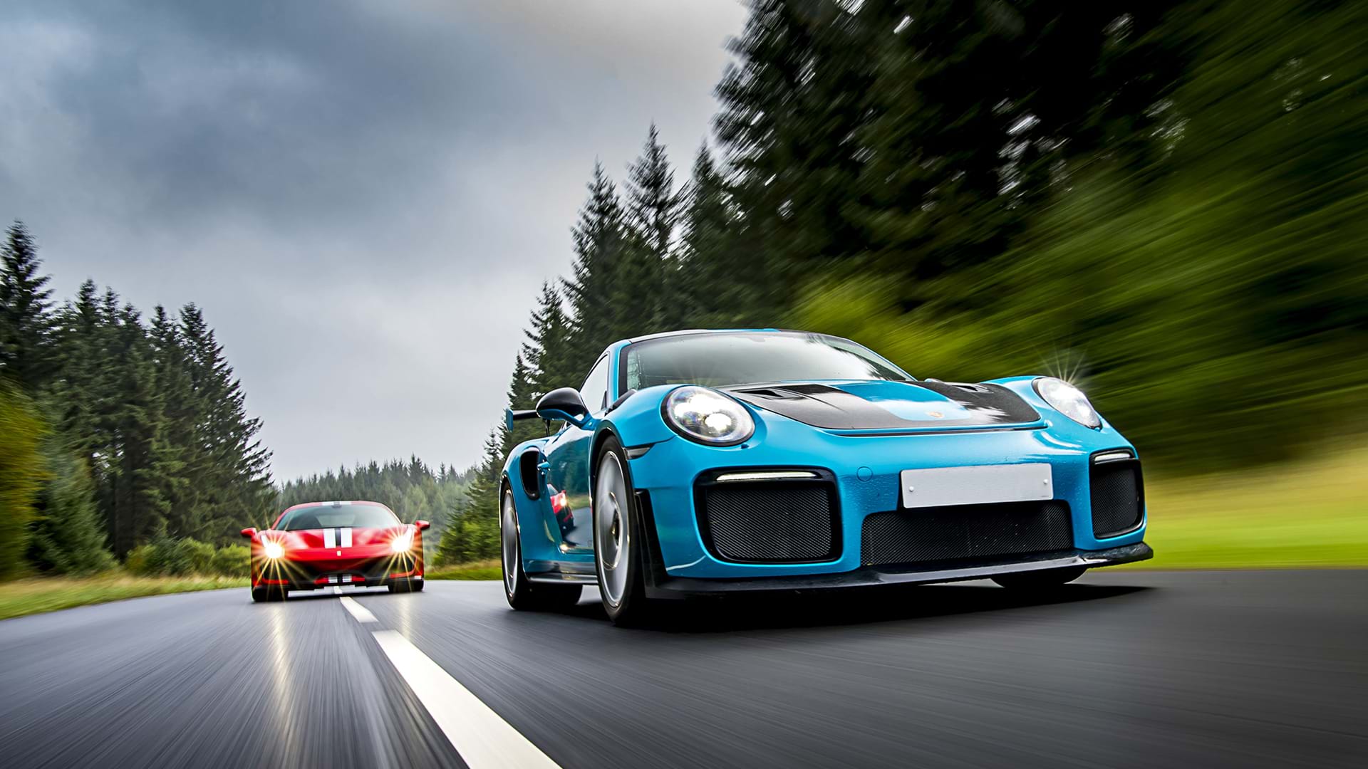 Porsche 991 GT3 RS blu che guida una Ferrari 488 Pista rossa su una strada panoramica. 